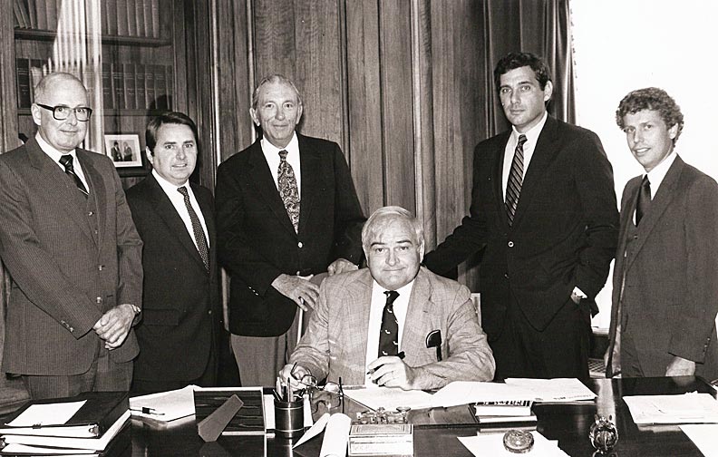 5 people standing behind one person seated at desk